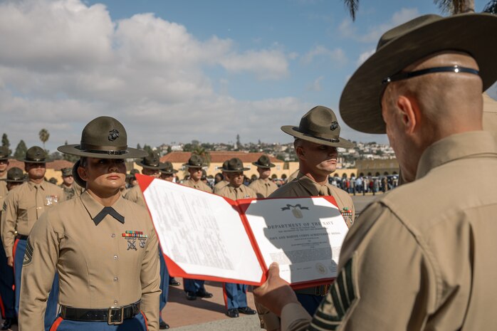 U.S. Marine Corps Drill Instructors, Staff Sgt. Burruel Delacruz, left, and Staff Sgt. Barry Clayton, back right, both with Charlie Company, 1st Recruit Training Battalion, are presented a Navy and Marine Corps Achievement Medal at Marine Corps Recruit Depot San Diego, California, Dec. 13, 2024. A NAM is given to members of the U.S. Navy and Marine Corps for meritorious service or achievement. Delacruz and Clayton received a NAM for exemplifying unrivaled courage and extraordinary presence of mind when confronting a life-threatening emergency. The words “drill instructor, drill instructor, drill instructor” were called and Delacruz and Clayton sprang into action to save a fourteen-month-old infant who was unconscious and not breathing. Providing CPR and proper throat sweeping techniques they successfully dislodged the obstruction and the infant regained consciousness. Likely saving baby Aisla’s life.  The family of the infant was onsite during the ceremony and presented the awards. The Marine Corps has served the Nation honorably for 250 years. Marines embody the uncompromising standards and characteristics of honor, courage and commitment.