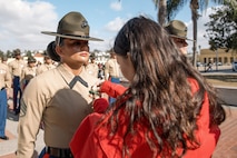 Baby Aisla’s mom, pins U.S. Marine Corps Drill Instructor, Staff Sgt. Burruel Delacruz, left, with Charlie Company, 1st Recruit Training Battalion, who is being presented with a Navy and Marine Corps Achievement Medal at Marine Corps Recruit Depot San Diego, California, Dec. 13, 2024. A NAM is given to members of the U.S. Navy and Marine Corps for meritorious service or achievement. Delacruz and Clayton received a NAM for exemplifying unrivaled courage and extraordinary presence of mind when confronting a life-threatening emergency. The words “drill instructor, drill instructor, drill instructor” were called and Delacruz and Clayton sprang into action to save a fourteen-month-old infant who was unconscious and not breathing. Providing CPR and proper throat sweeping techniques they successfully dislodged the obstruction and the infant regained consciousness. Likely saving baby Aisla’s life.  The family of the infant was onsite during the ceremony and presented the awards. The Marine Corps has served the Nation honorably for 250 years. Marines embody the uncompromising standards and characteristics of honor, courage and commitment.