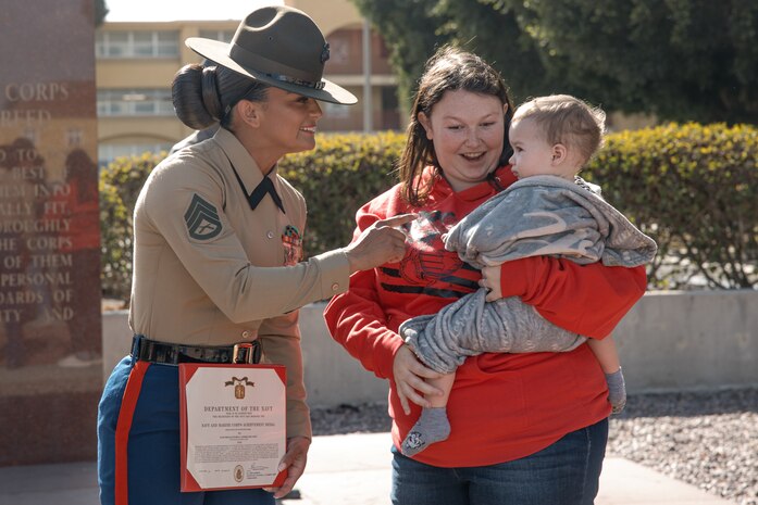 Baby Aisla and her mom, interact with U.S. Marine Corps Drill Instructor, Staff Sgt. Burruel Delacruz, left, with Charlie Company, 1st Recruit Training Battalion, after being presented with a Navy and Marine Corps Achievement Medal at Marine Corps Recruit Depot San Diego, California, Dec. 13, 2024. A NAM is given to members of the U.S. Navy and Marine Corps for meritorious service or achievement. Delacruz and Clayton received a NAM for exemplifying unrivaled courage and extraordinary presence of mind when confronting a life-threatening emergency. The words “drill instructor, drill instructor, drill instructor” were called and Delacruz and Clayton sprang into action to save a fourteen-month-old infant who was unconscious and not breathing. Providing CPR and proper throat sweeping techniques they successfully dislodged the obstruction and the infant regained consciousness. Likely saving baby Aisla’s life.  The family of the infant was onsite during the ceremony and presented the awards. The Marine Corps has served the Nation honorably for 250 years. Marines embody the uncompromising standards and characteristics of honor, courage and commitment.