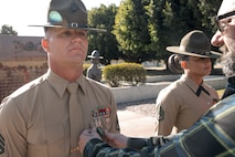 Baby Aisla’s grandpa, pins U.S. Marine Corps Drill Instructor, Staff Sgt. Barry Clayton, left, with Charlie Company, 1st Recruit Training Battalion, who is being presented with a Navy and Marine Corps Achievement Medal at Marine Corps Recruit Depot San Diego, California, Dec. 13, 2024. A NAM is given to members of the U.S. Navy and Marine Corps for meritorious service or achievement. Delacruz and Clayton received a NAM for exemplifying unrivaled courage and extraordinary presence of mind when confronting a life-threatening emergency. The words “drill instructor, drill instructor, drill instructor” were called and Delacruz and Clayton sprang into action to save a fourteen-month-old infant who was unconscious and not breathing. Providing CPR and proper throat sweeping techniques they successfully dislodged the obstruction and the infant regained consciousness. Likely saving baby Aisla’s life.  The family of the infant was onsite during the ceremony and presented the awards. The Marine Corps has served the Nation honorably for 250 years. Marines embody the uncompromising standards and characteristics of honor, courage and commitment.
