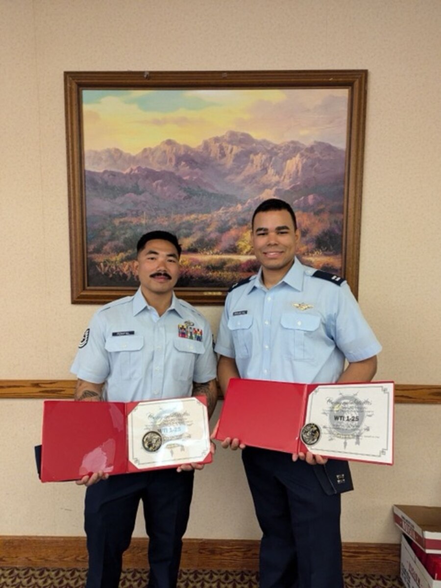 Two Airmen holding certificates after graduating a course