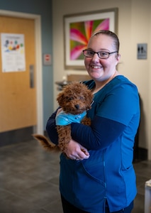 A woman wearing blue scrubs holds a small brown dog.