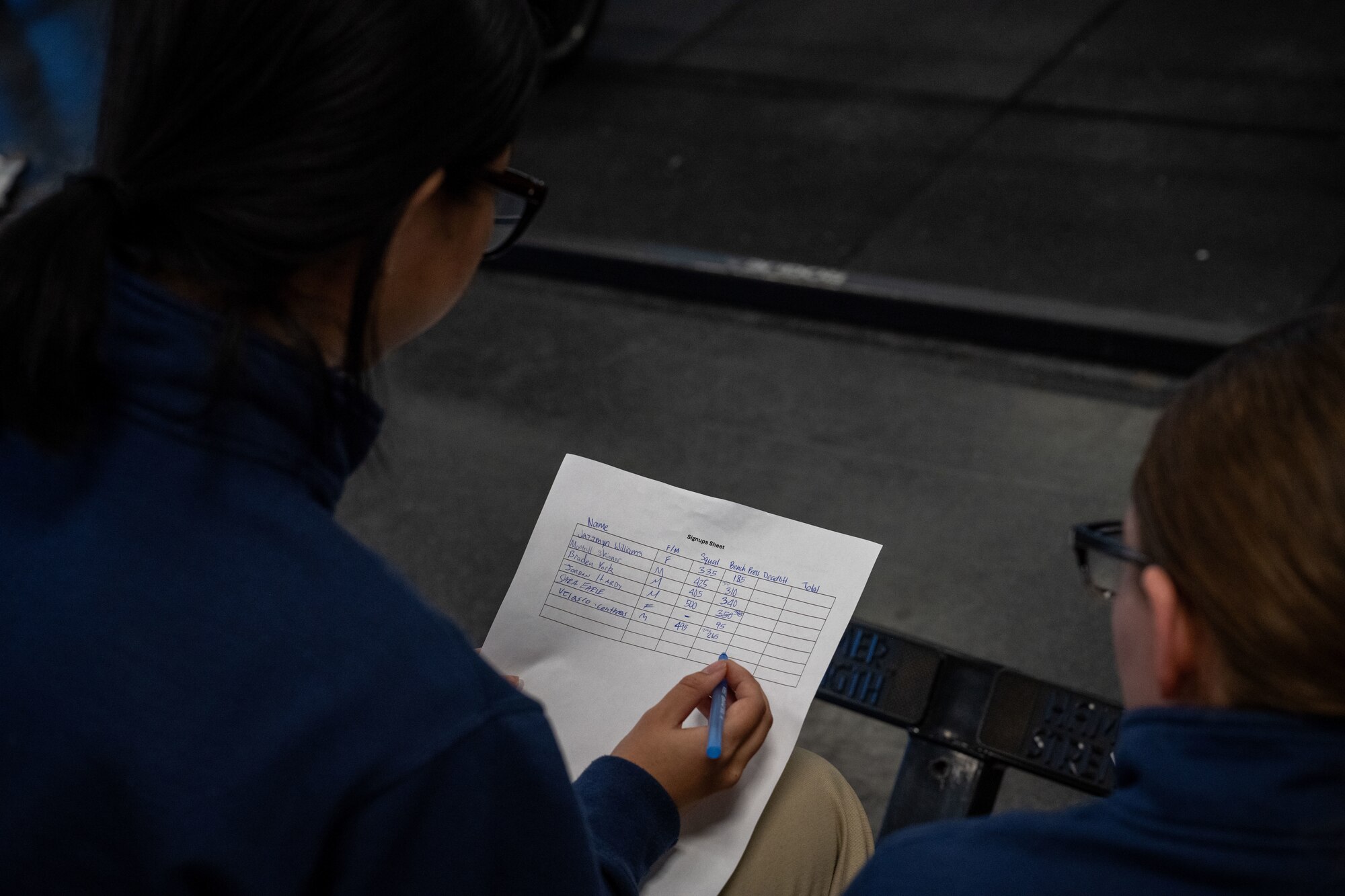 Airman 1st Class Chotirot Chuikrathok, 22nd Force Support Squadron fitness center apprentice and Senior Airman Shianne Garrison, 22nd Air Refueling Wing fitness associate track scores during a base weightlifting competition Dec. 11, 2024, at McConnell Air Force Base, Kansas. The 22nd Force Support Squadron hopes to make the weightlifting competition a recurring annual event. (U.S. Air Force photo by Airman 1st Class Paula Arce)