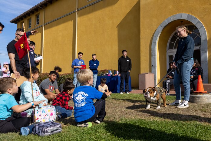U.S. Marine Corps Lance Cpl. Bruno, the Marine Corps Recruit Depot San Diego and Western Recruiting Region mascot and his handler Cpl. Sarah Grawcock, a combat photographer and the mascot handler, greets guests during a Devil Pups event at Marine Corps Recruit Depot San Diego, California, Dec. 14, 2024. The Devil Pups event is held in order to allow participants, aged five to twelve-years-old, to learn about Marine Corps culture, history, and traditions. This program is also a part of the Lifestyle, Insight, Network, Knowledge, and Skills Program, an interactive acculturation program to the Marine Corps lifestyle. (U.S. Marine Corps photo by Lance Cpl. Jacob B. Hutchinson)