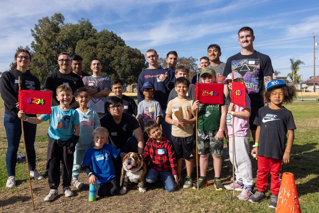 Participants and volunteers pose for a photo with U.S. Marine Corps Lance Cpl. Bruno, the Marine Corps Recruit Depot San Diego and Western Recruiting Region mascot, after a Devil Pups event at Marine Corps Recruit Depot San Diego, California, Dec. 14, 2024. The Devil Pups event is held in order to allow participants, aged five to twelve-years-old, to learn about Marine Corps culture, history, and traditions. This program is also a part of the Lifestyle, Insight, Network, Knowledge, and Skills Program, an interactive acculturation program to the Marine Corps lifestyle. (U.S. Marine Corps photo by Lance Cpl. Jacob B. Hutchinson)