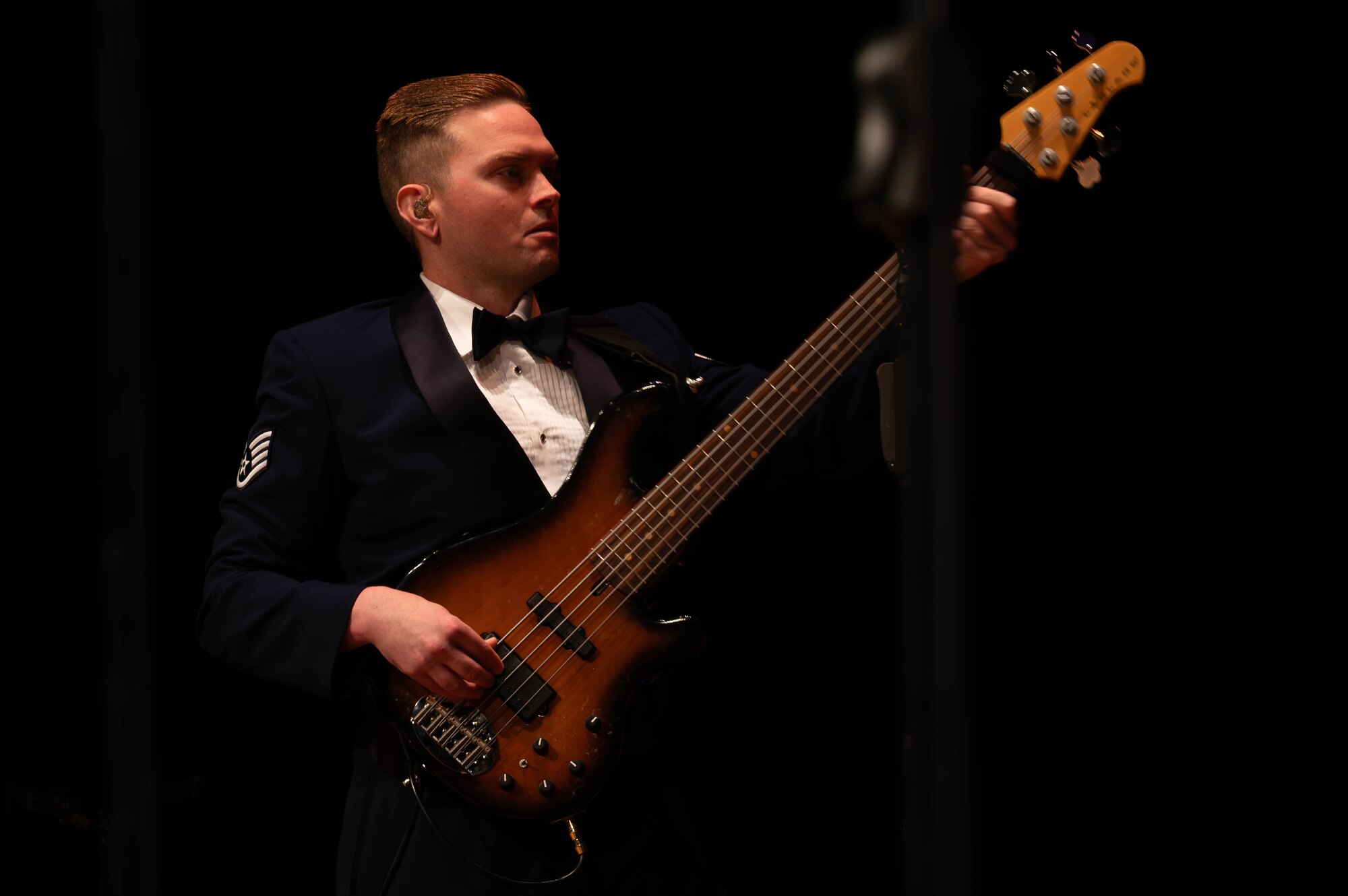 Bass guitarist's face is in focus as he plays on stage looking at his hands.