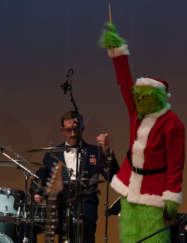 The Grinch stands over the drummer with his drumstick in hand facing the towards the audience.