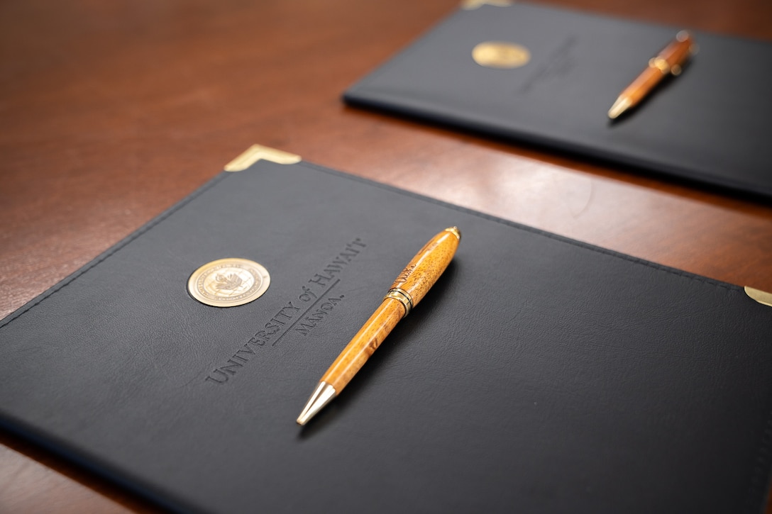 Two copies of an updated memorandum of agreement sit on a desk at a signing ceremony at the University of Hawai’i at Mānoa in Honolulu, Hawaii, Dec. 19, 2024. Coast Guard Rear Adm. Sean Regan, commander of District Fourteen, and Michael Bruno, provost at UH Mānoa, signed the MOA to continue the College Student Pre-Commissioning Initiative scholarship program at UH Mānoa. (U.S. Coast Guard photo by Petty Officer 2nd Class Tyler Robertson)