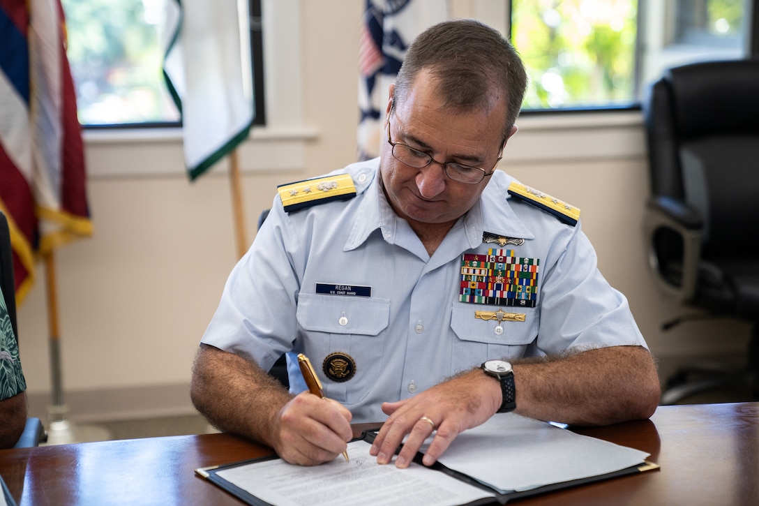 Coast Guard Rear Adm. Sean Regan, commander of District Fourteen, signs an updated memorandum of agreement to continue the College Student Pre-Commissioning Initiative scholarship program at UH Mānoa in Honolulu, Hawaii, Dec. 19, 2024. The Coast Guard CSPI program pays for up to two academic years of college tuition for eligible students at minority-serving institutions. (U.S. Coast Guard photo by Petty Officer 2nd Class Tyler Robertson)