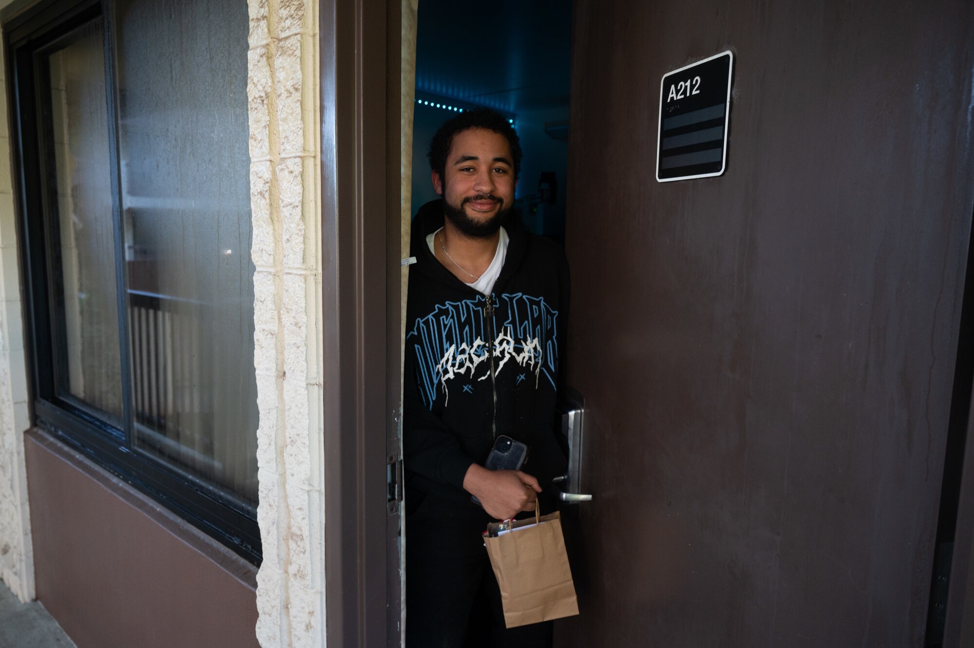 An airman opens his door to his dorm with a bag in his hand.