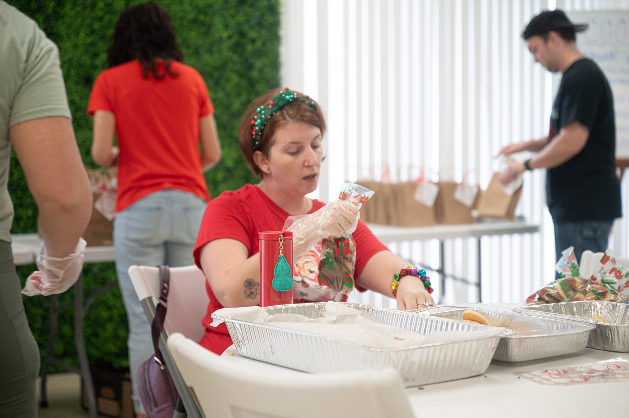 A woman dressed in holiday decor holds a bag of cookies while sitting down.