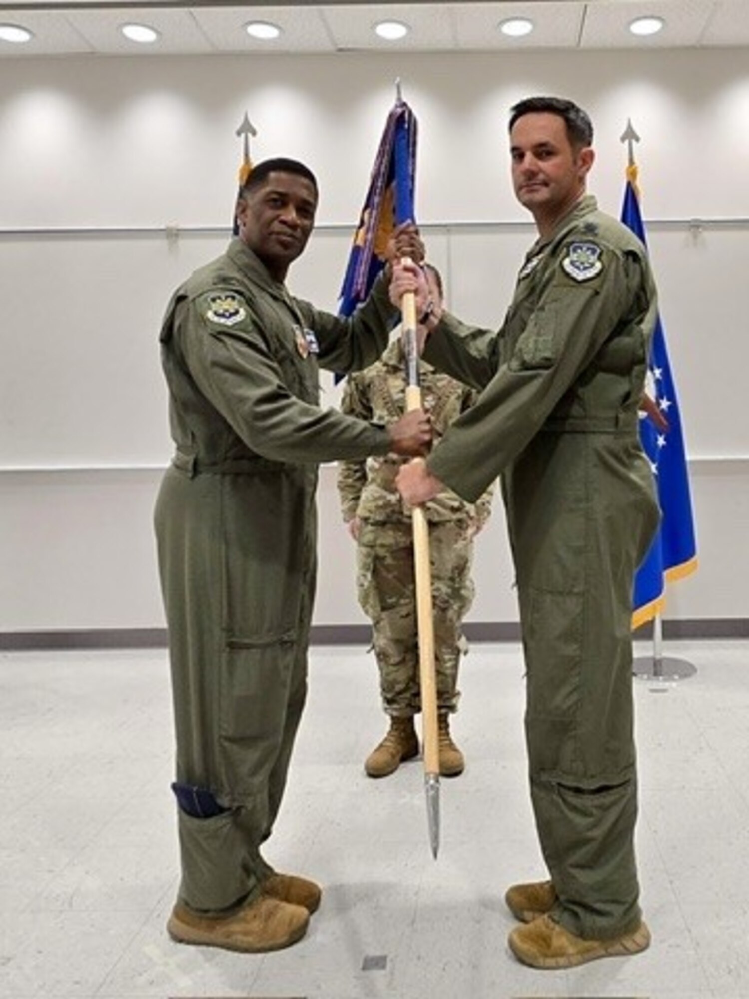 photo of two uniformed U.S. Air Force Airmen standing, holding a unit flag between them