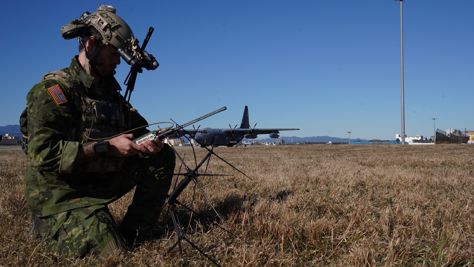 An Airman kneels on the ground to operate communications equipment.