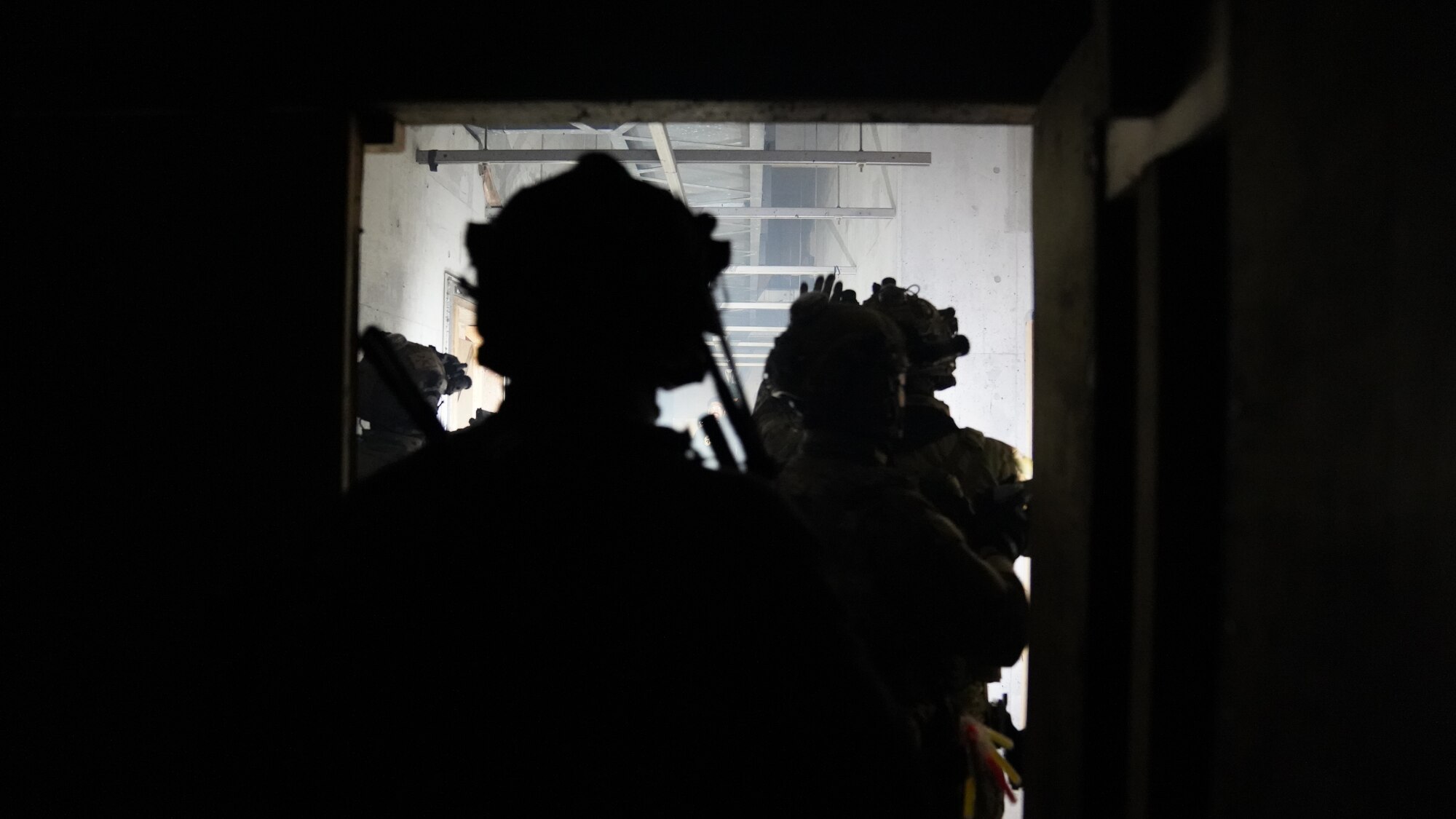 Military operators stand in a stacked formation while clearing a building.