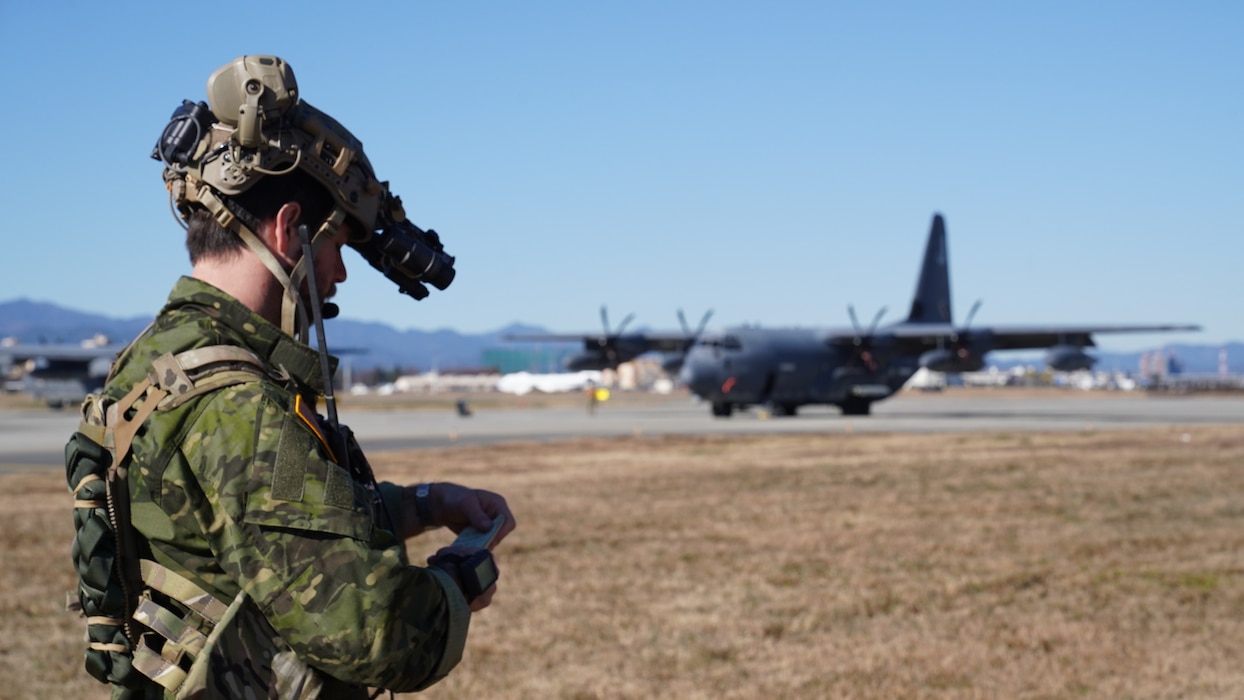 An Airman looks operates a communications device in front of an MC-130J taxing on an airfield.