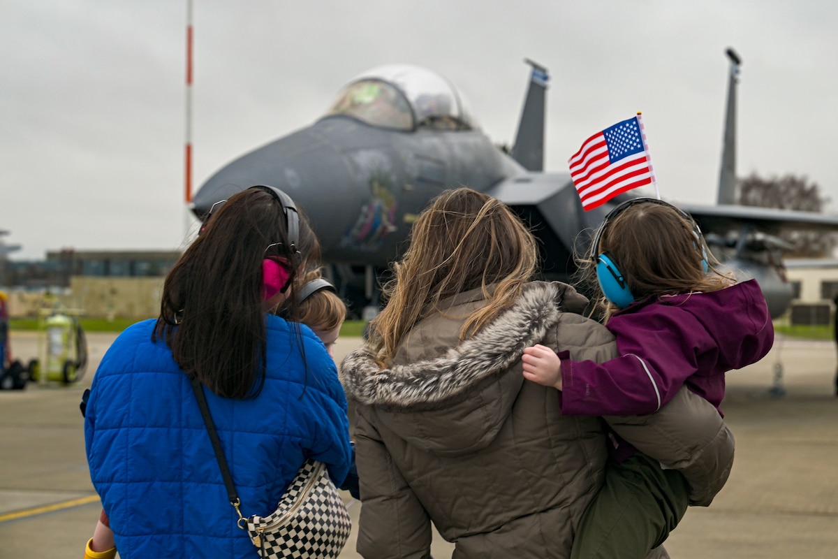 Two women wait with their children for their spouses to deplane an F-15.