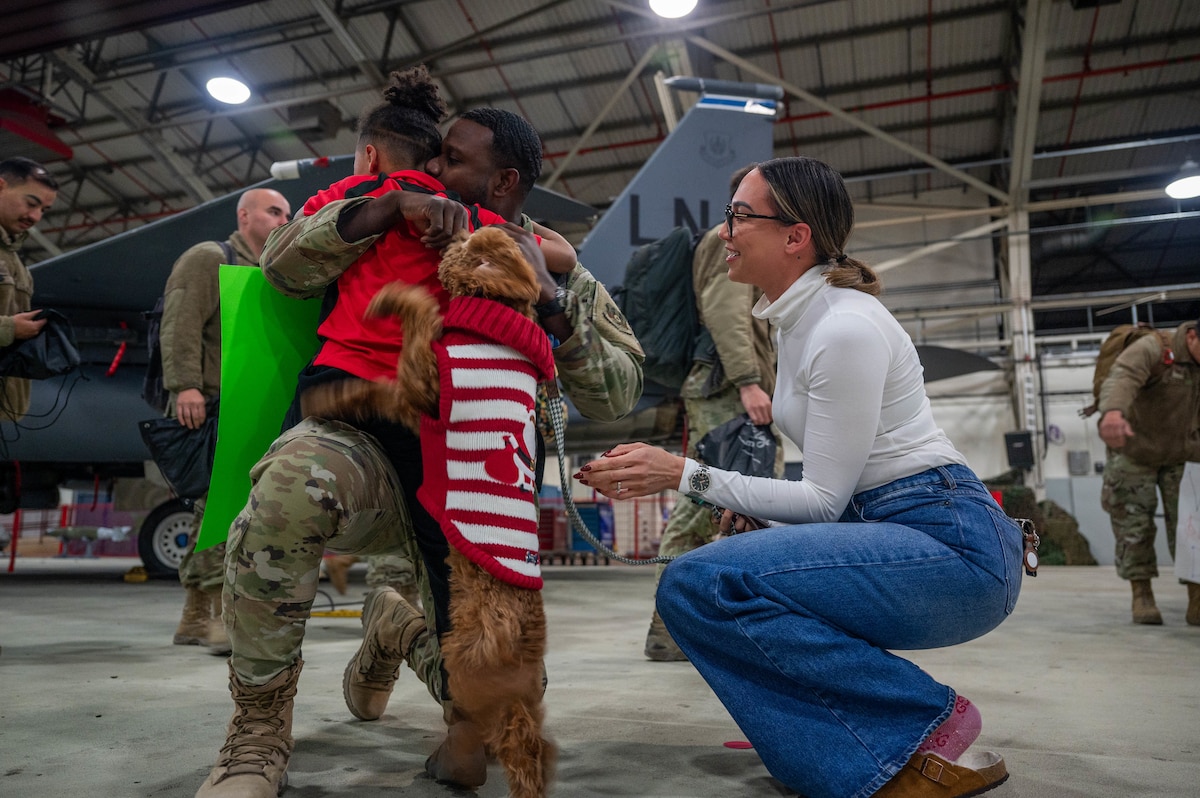 Man kneels to hug his son, dog and wife.