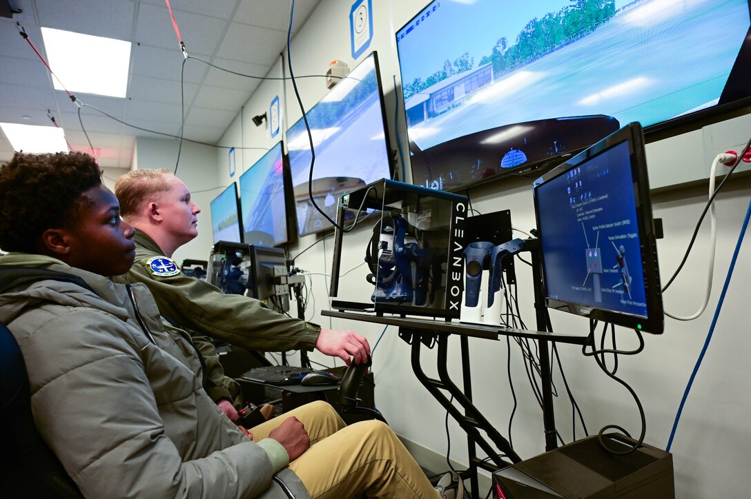 A U.S. Airman works a flight simulator with a teenager