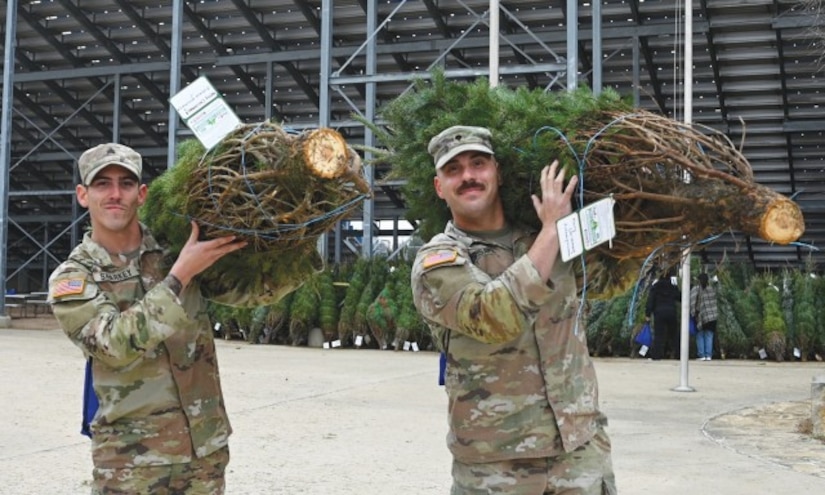 Two soldiers carry Christmas trees away from the stands of a stadium.