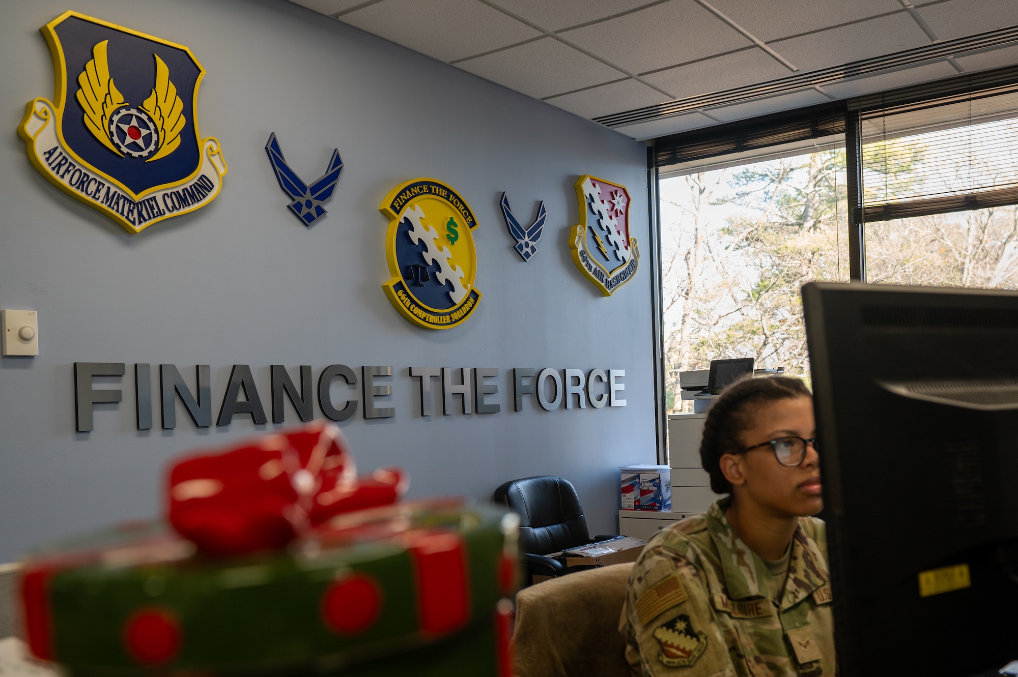 Airman sitting at a computer with unit symbols behind her.