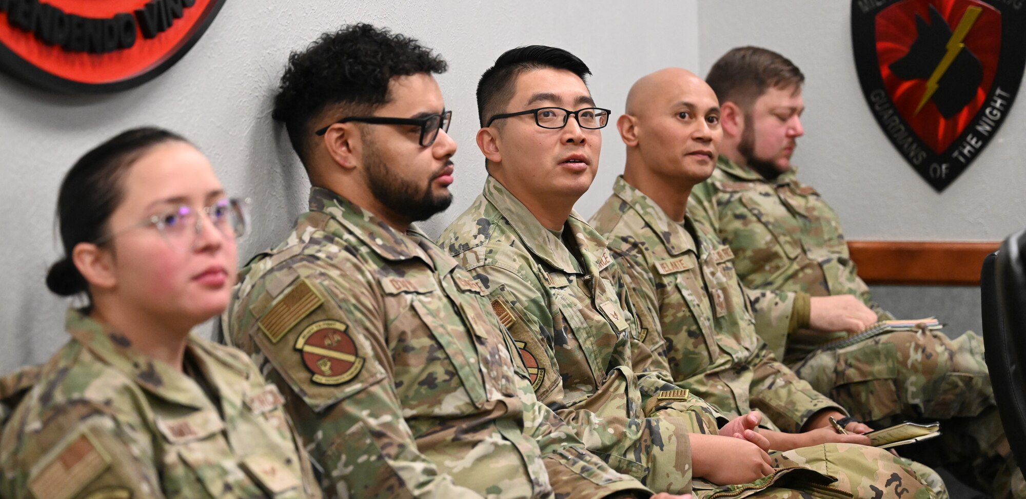 21st Security Forces members participating in the exchange participate in a staff meeting sitting along the wall.