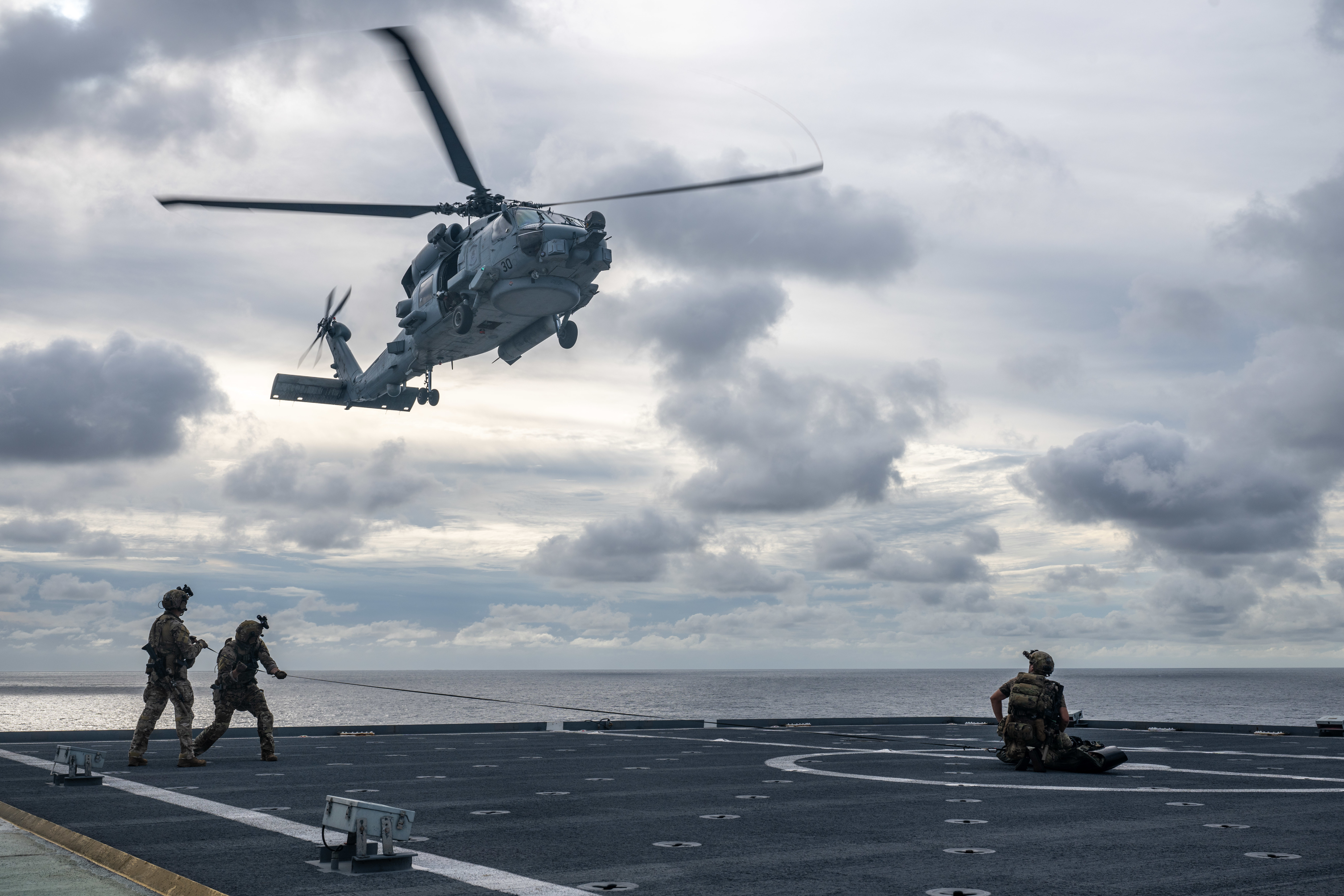 A U.S. Naval Special Warfare operator and U.S. Coast Guard Maritime Security Response Team (West) members prepare for an MH-60R Seahawk helicopter from the "Magicians" of Helicopter Maritime Strike Squadron (HSM) 35 to pick up a simulated casualty aboard the 2nd Lt. John P. Bobo-class cargo ship USNS PFC Dewayne T. Williams (T-AK 3009) during visit, board, search, and seizure training in the Andaman Sea, Dec. 15, 2024.