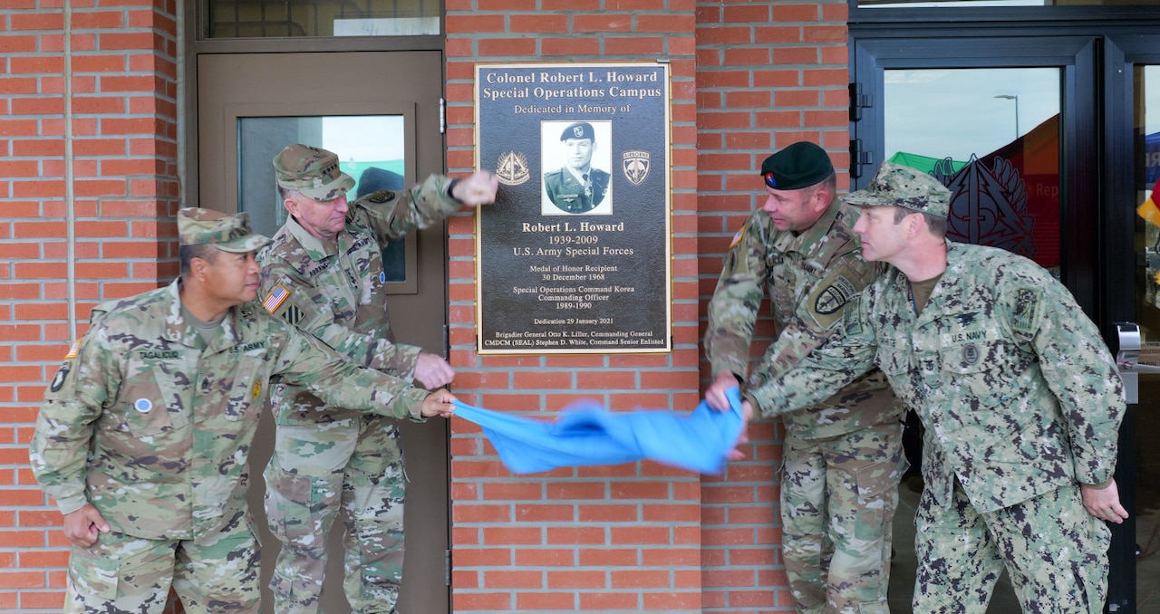 Four men pull a cover off a plaque attached to a wall.