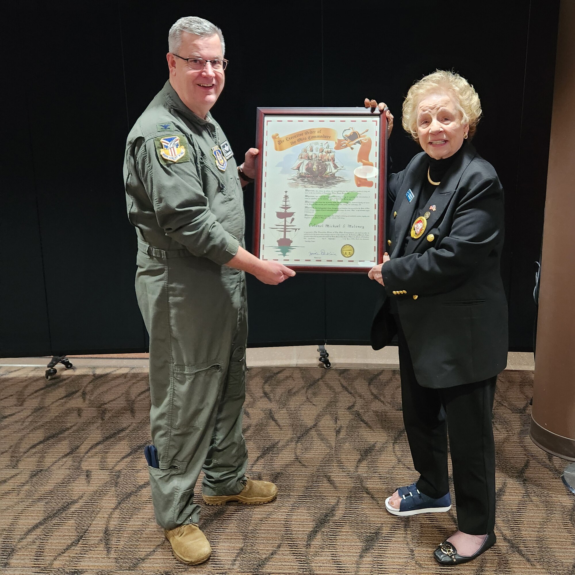 Col. Mike Maloney, 910th Airlift Wing commander, poses for a photo while holding a framed memento with Ginni Ragan, a trustee of the board of the Association of Ohio Commodores.