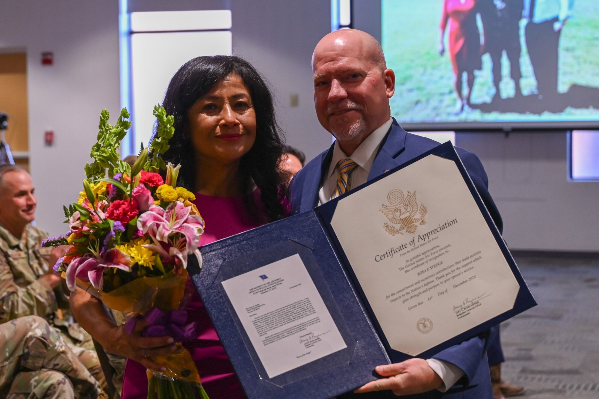 Special Agent Lynn Stedge, Office of Special Investigations Operating Location-B director, right, and Rosa Stedge, his spouse, pose for a photo with her certificate of appreciation during his retirement ceremony at Davis-Monthan Air Force Base, Arizona, Dec.19, 2024. Stedge retired after a combined 37 years of both military and civilian service. (U.S. Air Force photo by Senior Airman Andrew Garavito)