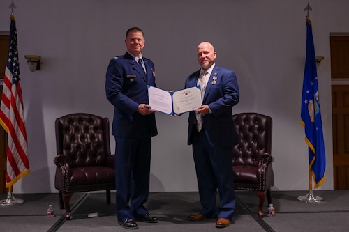 U.S. Air Force Col. Andrew Schad, Office of Special Investigations reserve advisor, left, and Agent Lynn Stedge, OSI Operating Location-B director, pose during a retirement ceremony at Davis-Monthan Air Force Base, Arizona, Dec.19, 2024. OSI was created in 1948 and defends the Nation, pursues justice, protects the Department of the Air Force and finds the truth. (U.S. Air Force photo by Senior Airman Andrew Garavito)