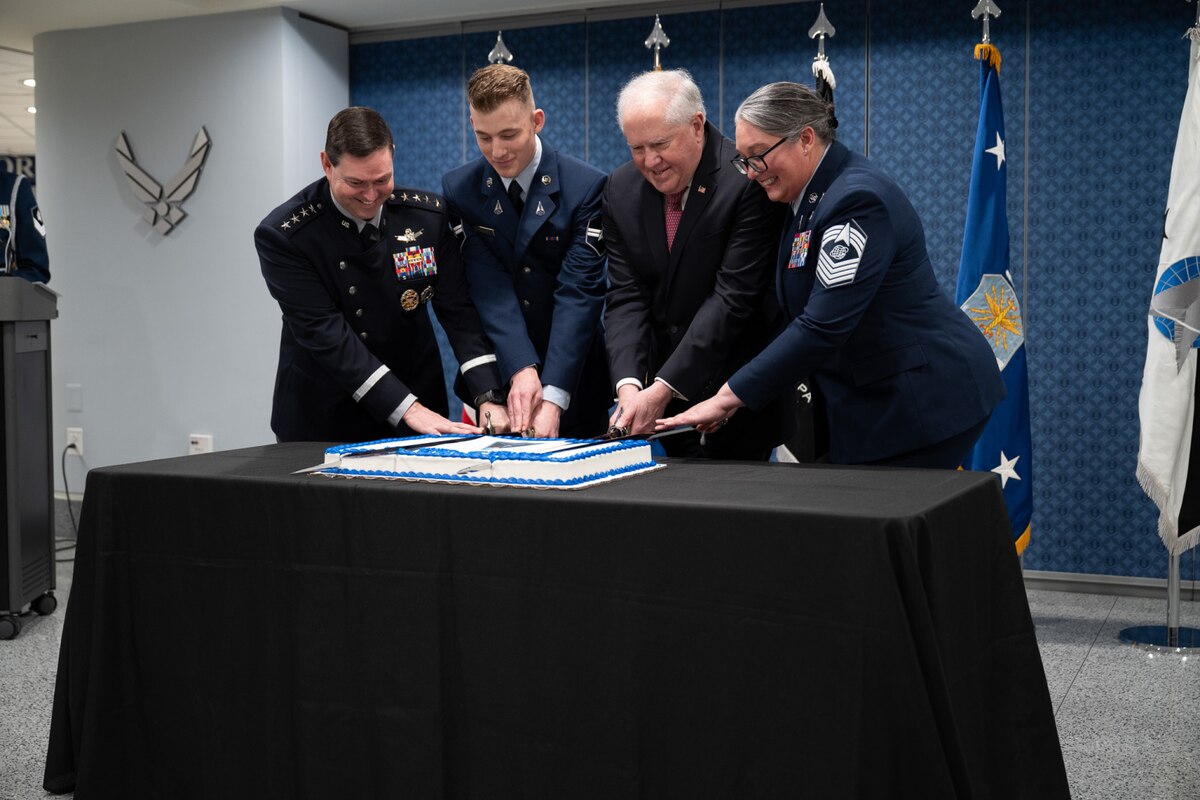 Four people, some in uniforms, use swords to cut a cake.