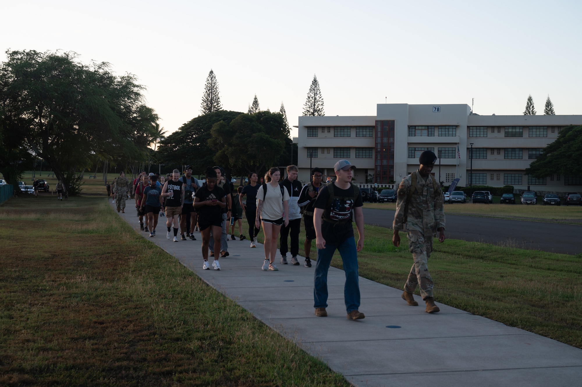Military personnel walk together in a group during the sunrise on a pave path.
