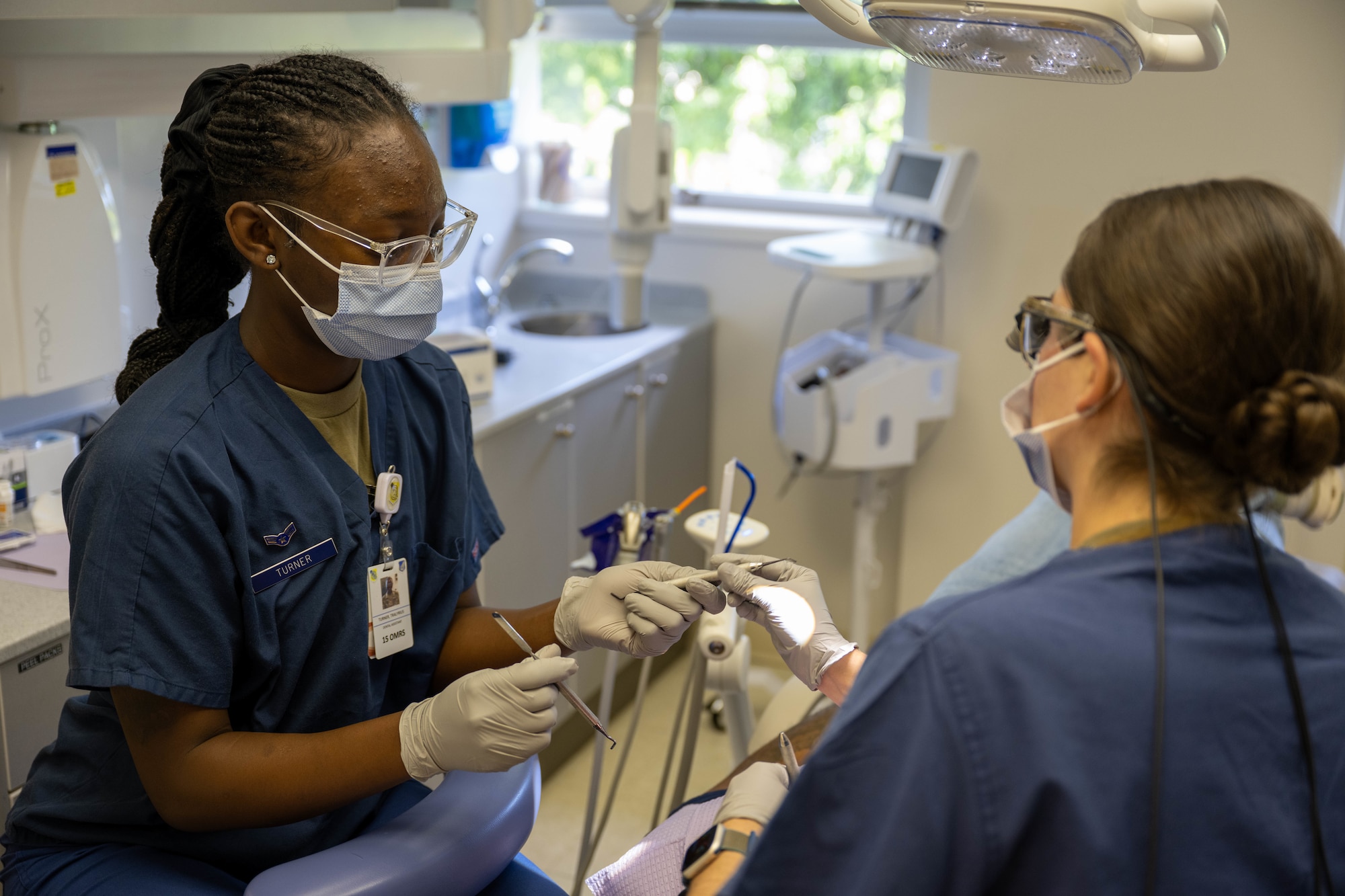 A dental assistant hands a dentist a oral tool who is examining a patient's teeth.