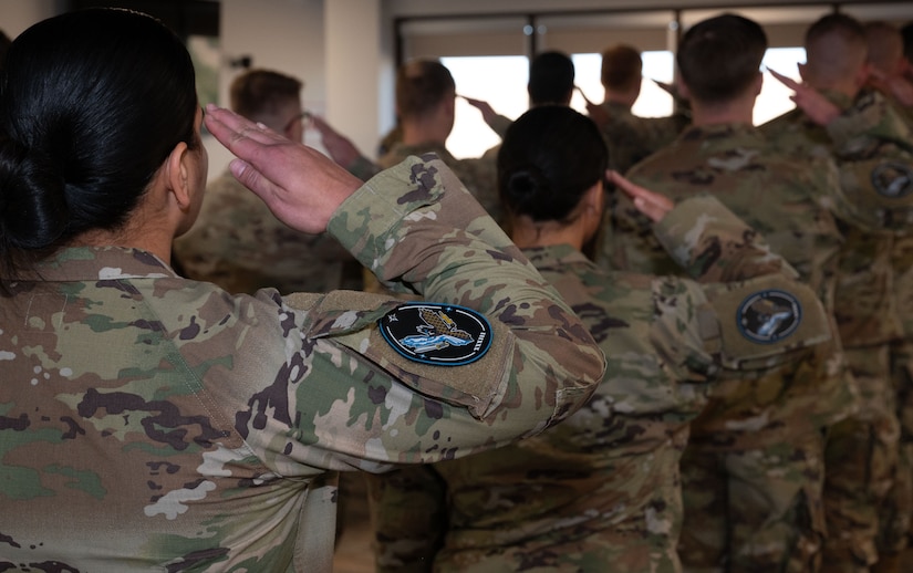 Guardians, shown from behind, salute while standing in formation indoors.