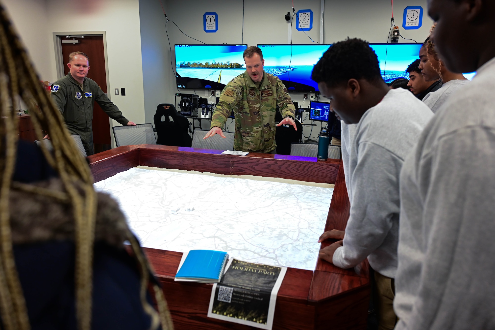 U.S. Airmen and teenagers stand around a sand table