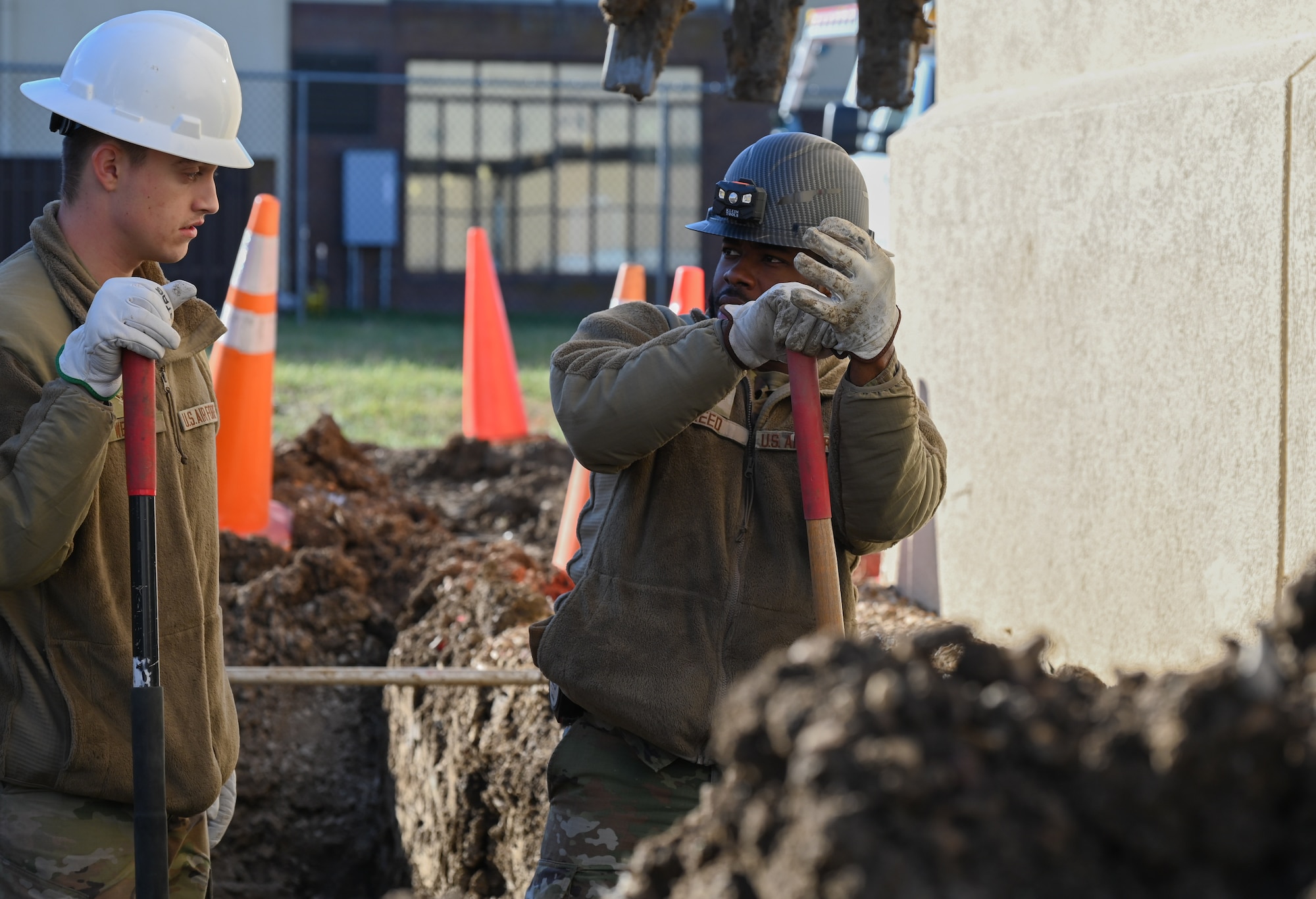 U.S. Air Force Senior Airman Imani Reed and Airman Ethan Welsh, 509th Civil Engineer Squadron electrical systems apprentices, excavate around pipes and wires at Whiteman Air Force Base, Mo., Dec. 7, 2023. Reed and Welsh are clearing the way to connect the water treatment facility to back up and emergency power. (U.S. Air Force Photo by Airman 1st Class Matthew S. Domingos)