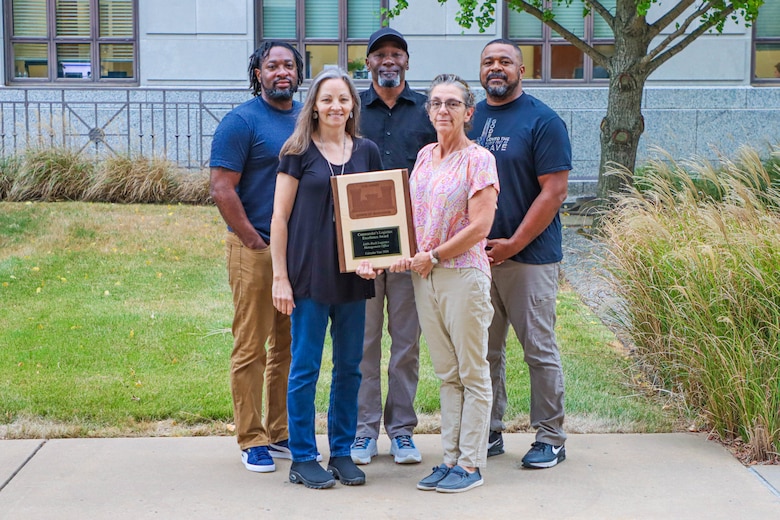 two women and three men standing together with one holding an award.