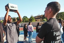 U.S. Marine Corps Pvt. Yair Beatriz, a recruiter assistant with Recruiting Sub-Station Hemet, Recruiting Station San Diego, oversees a student performing ammo can lifts during a weight room takeover at Beaumont High School in Beaumont, California, Dec. 16, 2024. A weight room takeover is an event where Marines engage with students in a gym setting, leading workouts and demonstrating fitness techniques as part of a community outreach or recruitment effort. (U.S. Marine Corps photo by Cpl. Alejandro Fernandez)