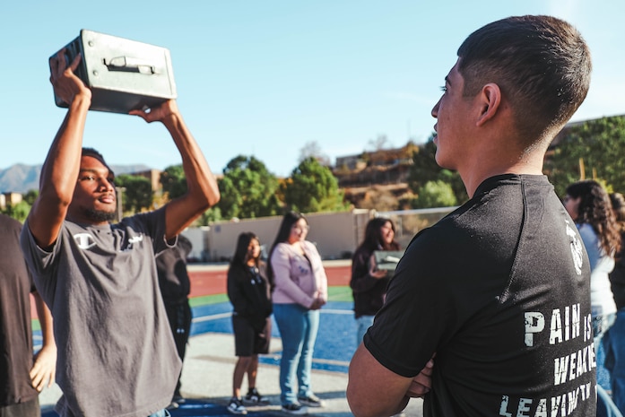 U.S. Marine Corps Pvt. Yair Beatriz, a recruiter assistant with Recruiting Sub-Station Hemet, Recruiting Station San Diego, oversees a student performing ammo can lifts during a weight room takeover at Beaumont High School in Beaumont, California, Dec. 16, 2024. A weight room takeover is an event where Marines engage with students in a gym setting, leading workouts and demonstrating fitness techniques as part of a community outreach or recruitment effort. (U.S. Marine Corps photo by Cpl. Alejandro Fernandez)