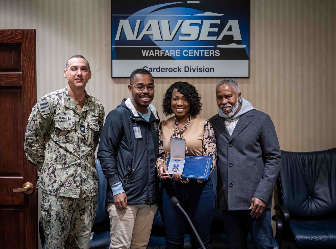 Carderock Commanding Officer, Capt. Chris Matassa, presents Lisa A. Harden with the Department of the Navy Meritorious Civilian Service Award alongside her son and husband at Naval Surface Warfare Center Carderock Division