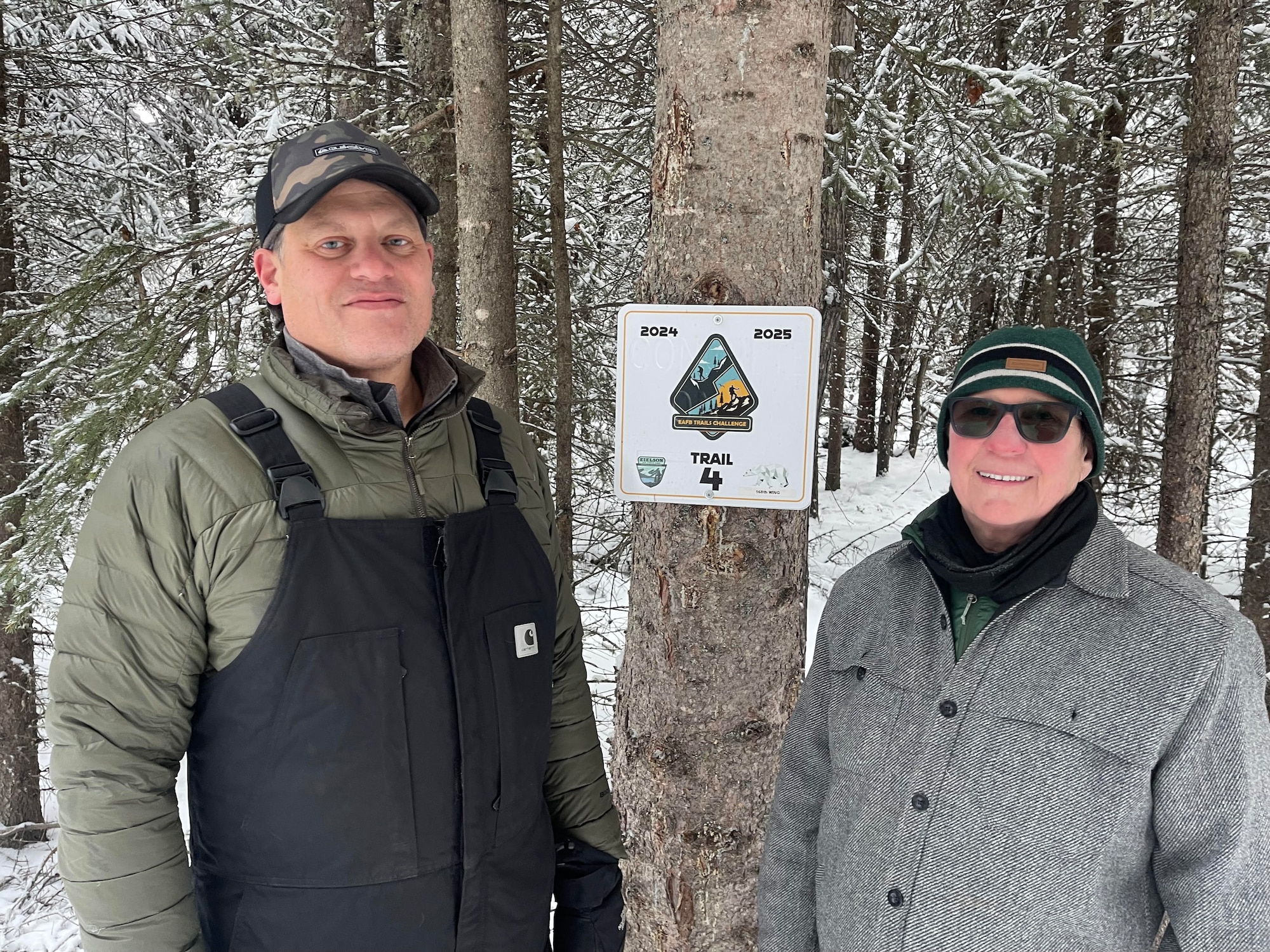 Gene Larocca of the Eielson Air Force Base Natural Resources and Deb Lipyanic of the Alaska Air National Guard, 168th Wing Environmental office stand in front of the new Winter Trails Challenge sign, posing for a photo to kick off the hiking and skiing challenge.