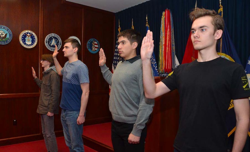 Four people in civilian cloths stand in a row with their right hands raised.