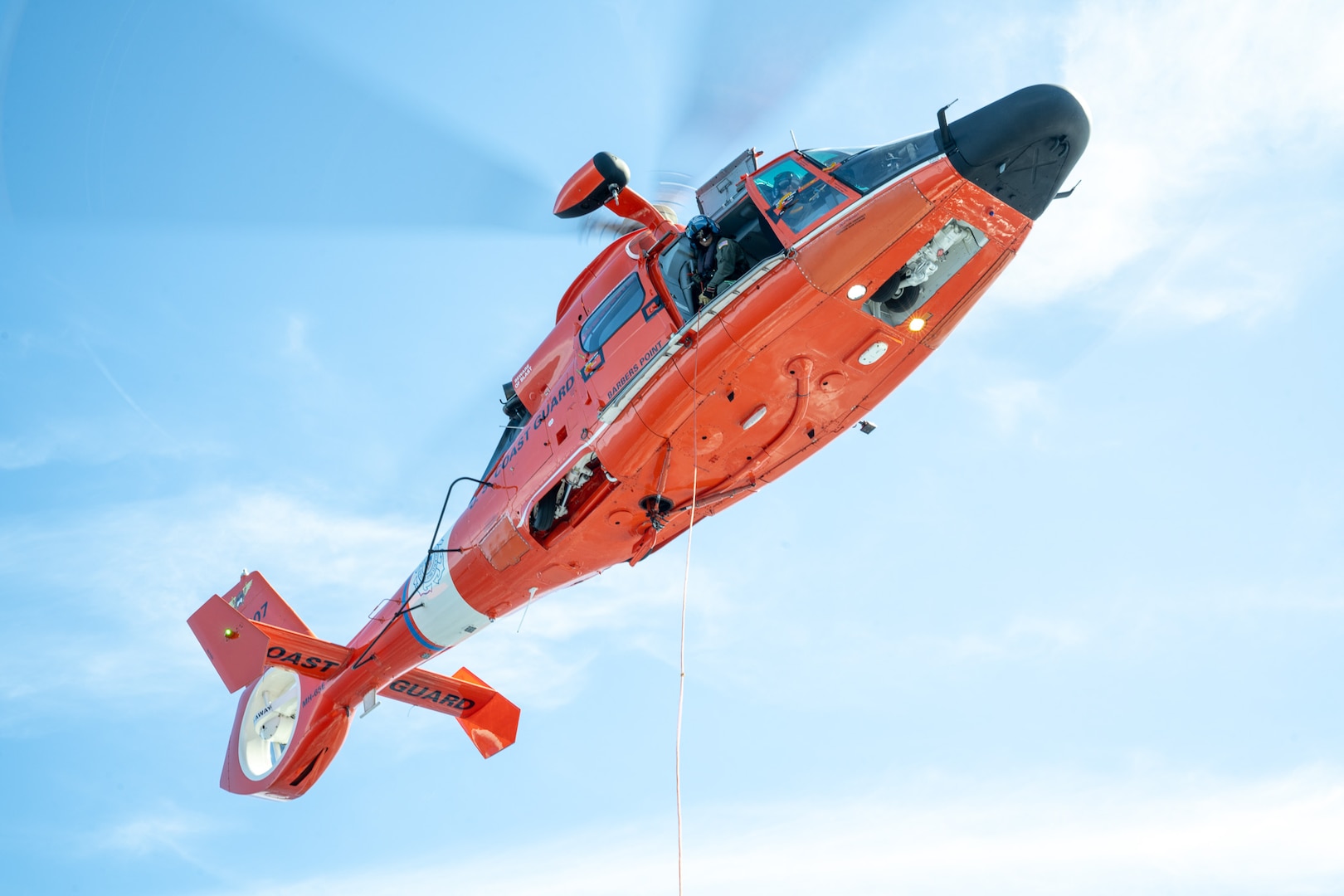 A Coast Guard MH-65 Dolphin helicopter crew assigned to Air Station Barbers Point, deploys a tending line to an underway vessel while conducting training off the north shore of Oahu Dec. 3, 2024. The helicopter crew conducted training deploying supplies and gear to an underway vessel. (U.S. Coast Guard photo by Petty Officer 2nd Class Tyler Robertson)