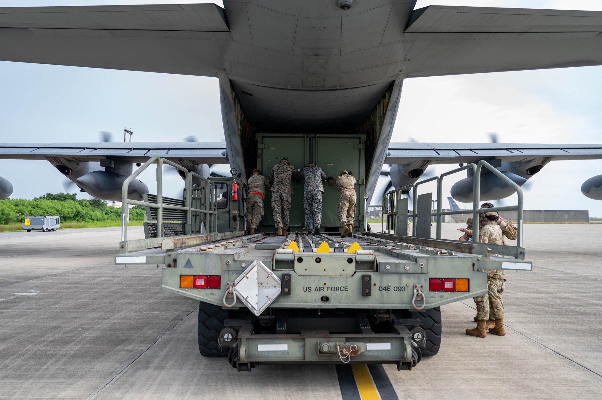Service members push cargo into plane.
