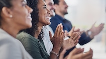 A close-up image of diverse women and men applauding for a speaker at a business conference