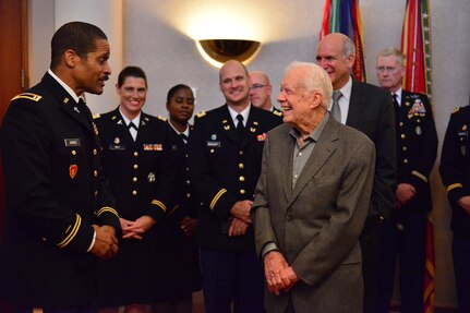 President Jimmy Carter stands on the right smiling while facing a Georgia National Guardsman