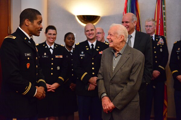 President Jimmy Carter stands on the right smiling while facing a Georgia National Guardsman