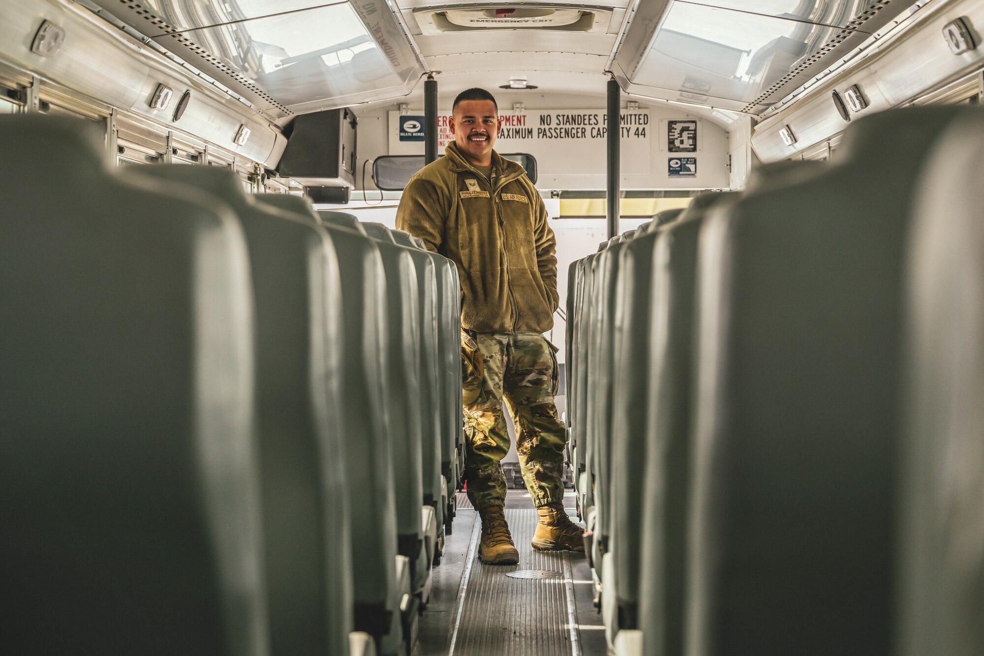 A man in uniform stands in a bus walkway posing for a photo.