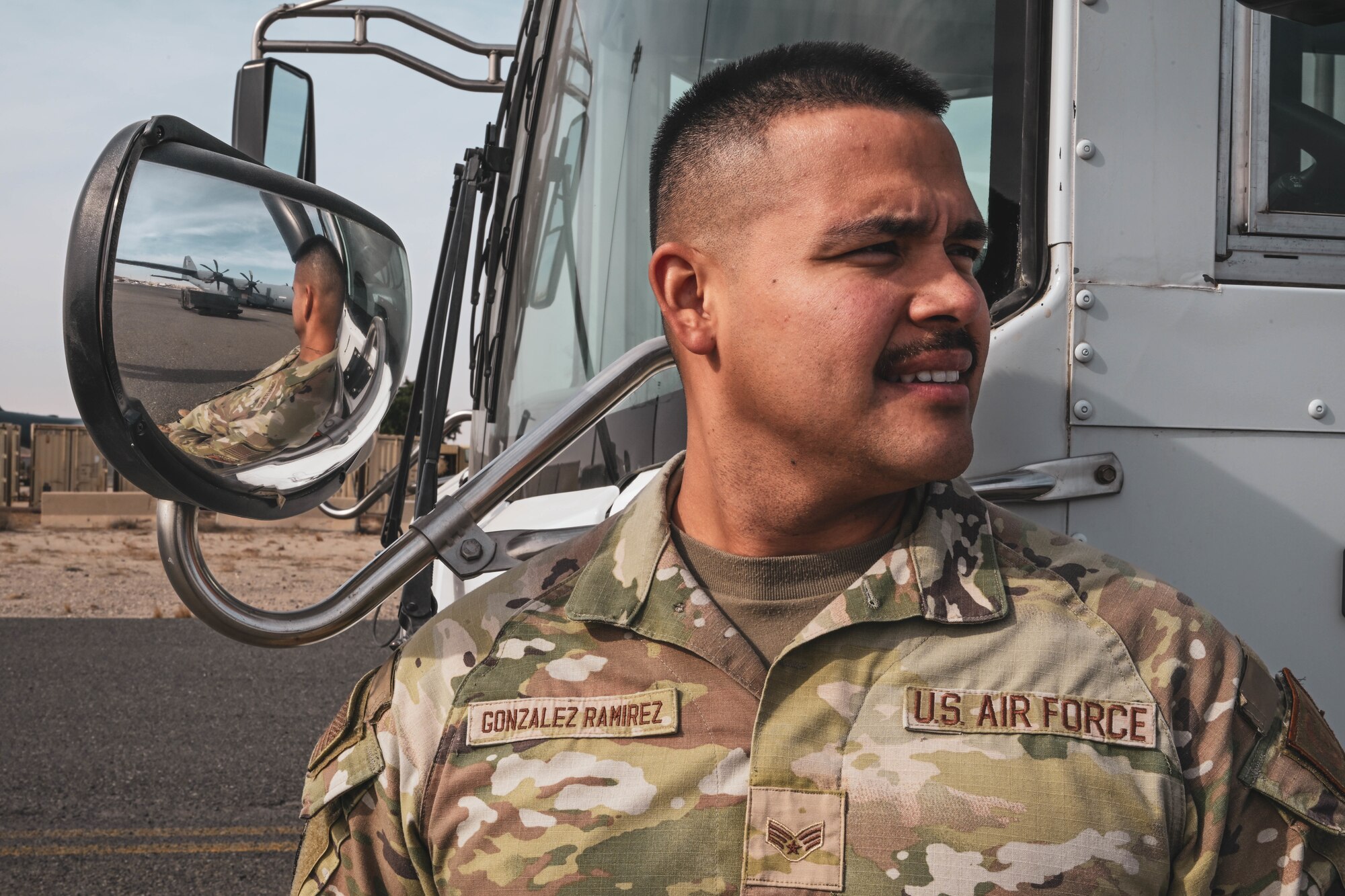 A man in uniform stands in front of a bus mirror.
