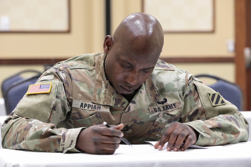 A uniformed soldier sits and writes at a table.